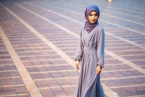 Portrait of a woman in a purple hijab and dress walking at a Jakarta landmark.