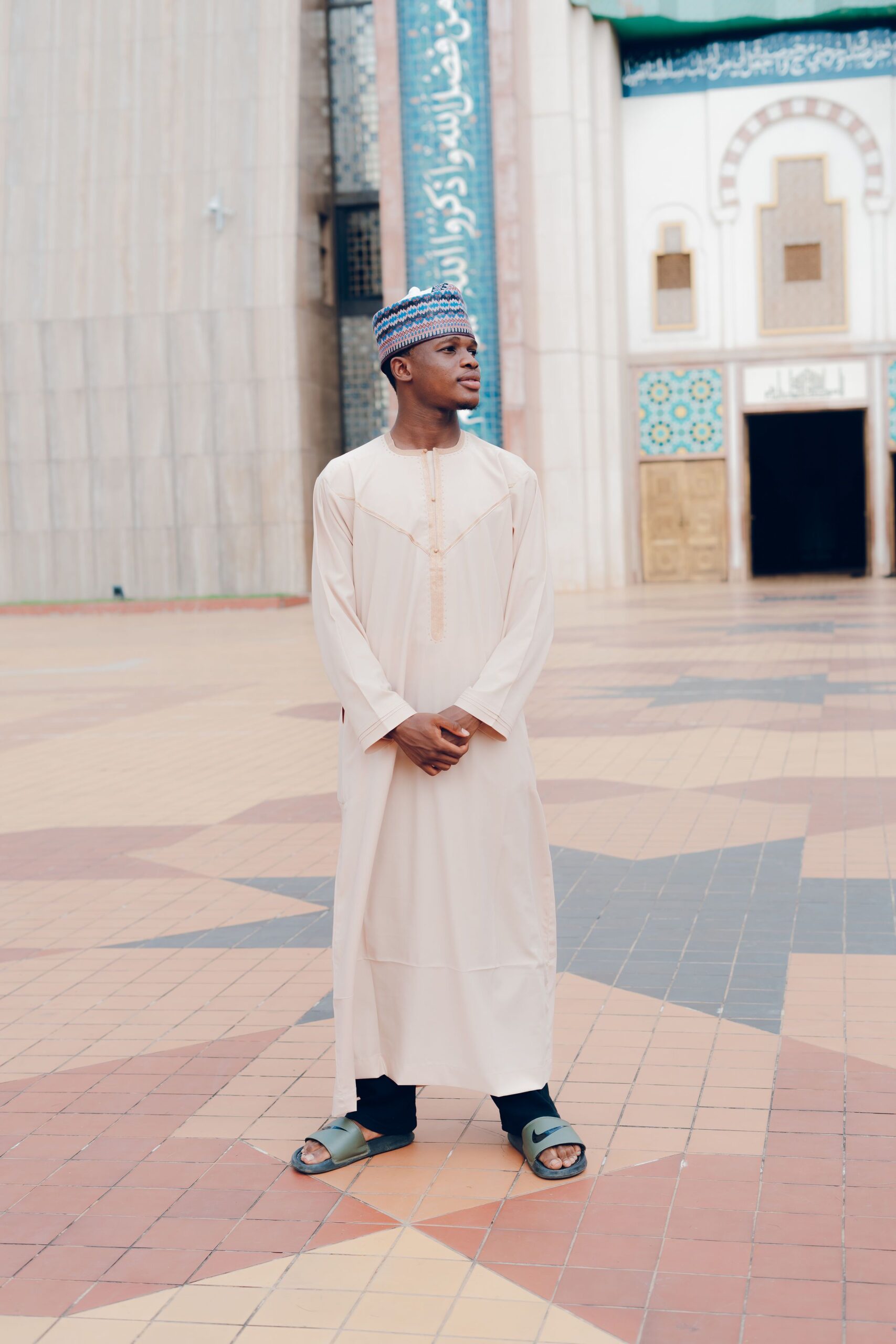 Man stands in traditional attire at mosque courtyard, embracing cultural heritage.